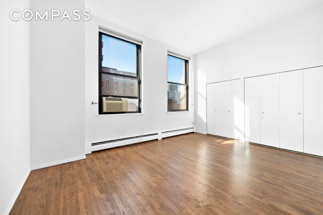 unfurnished bedroom featuring multiple closets, hardwood / wood-style floors, and baseboard heating