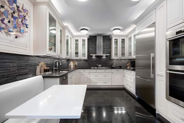 kitchen featuring wall chimney range hood, decorative backsplash, stainless steel appliances, and a sink