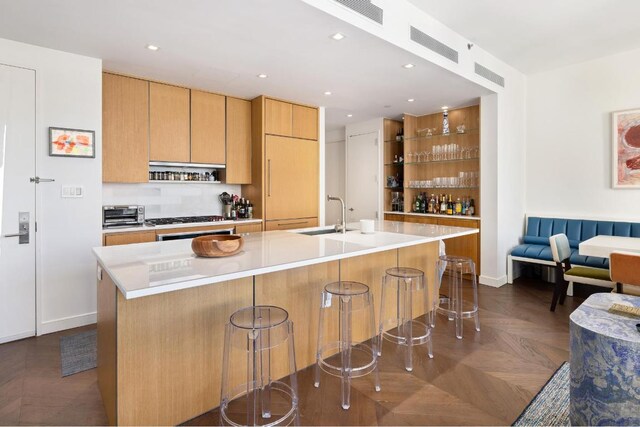 kitchen with dark parquet flooring, sink, a breakfast bar area, and a kitchen island with sink