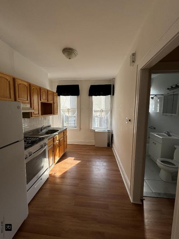 kitchen with white appliances, baseboards, decorative backsplash, dark wood-style floors, and a sink