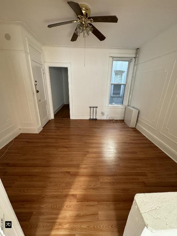 empty room with ceiling fan, a decorative wall, and dark wood-style flooring