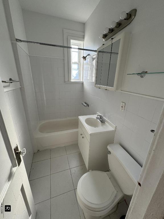 full bathroom featuring tile patterned flooring, tile walls, vanity, tiled shower / bath, and toilet