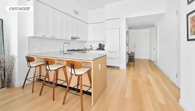 kitchen with white cabinetry, sink, kitchen peninsula, and a kitchen bar