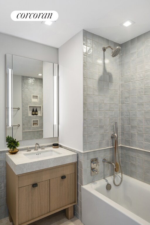 bathroom with tiled shower / bath, vanity, and tile walls