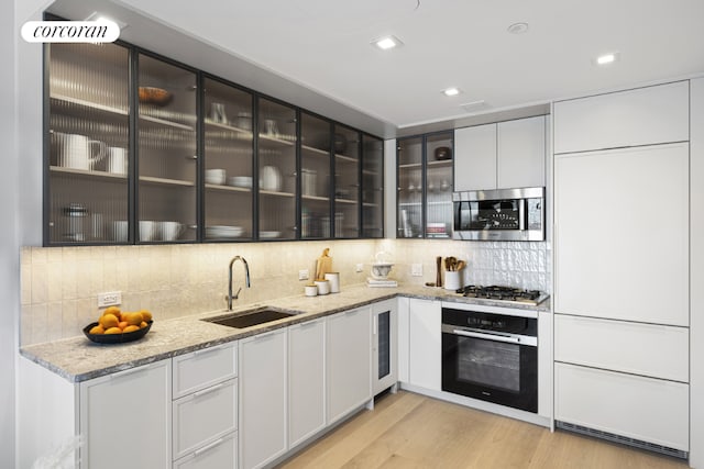 kitchen featuring sink, light stone counters, light hardwood / wood-style flooring, appliances with stainless steel finishes, and white cabinets