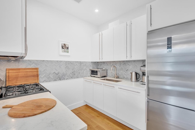 kitchen with light countertops, built in refrigerator, a sink, and white cabinets