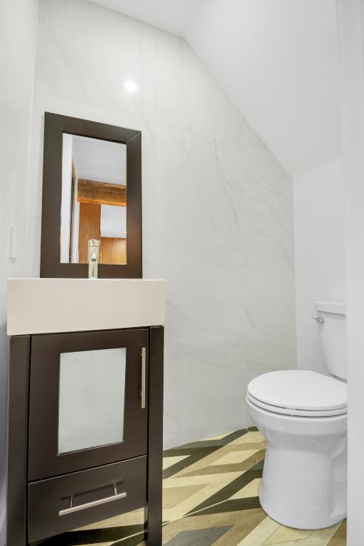 bathroom with vaulted ceiling, tile walls, vanity, and toilet