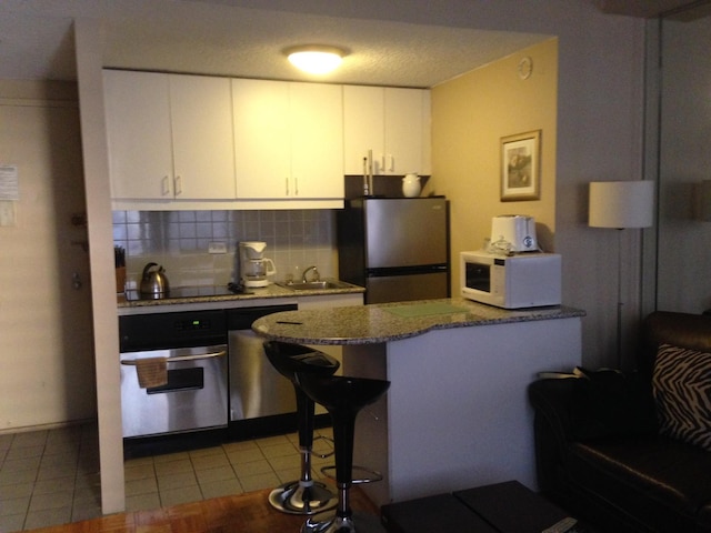 kitchen with a peninsula, stone countertops, stainless steel appliances, white cabinetry, and tasteful backsplash