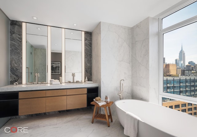 555 W 22nd St Unit Ph16Be, New York City, NY 10011 - bathroom featuring marble tiled floors, stone wall, vanity, a view of city, and a freestanding tub
