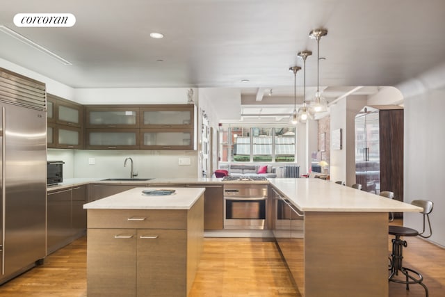 kitchen with sink, a breakfast bar, stainless steel appliances, a kitchen island, and decorative light fixtures