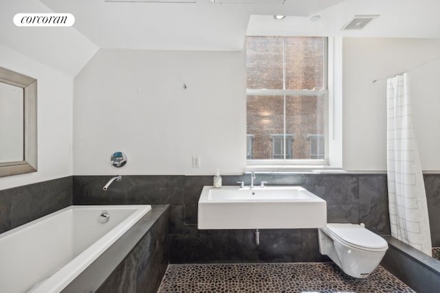 bathroom with toilet, sink, vaulted ceiling, tile walls, and tiled tub