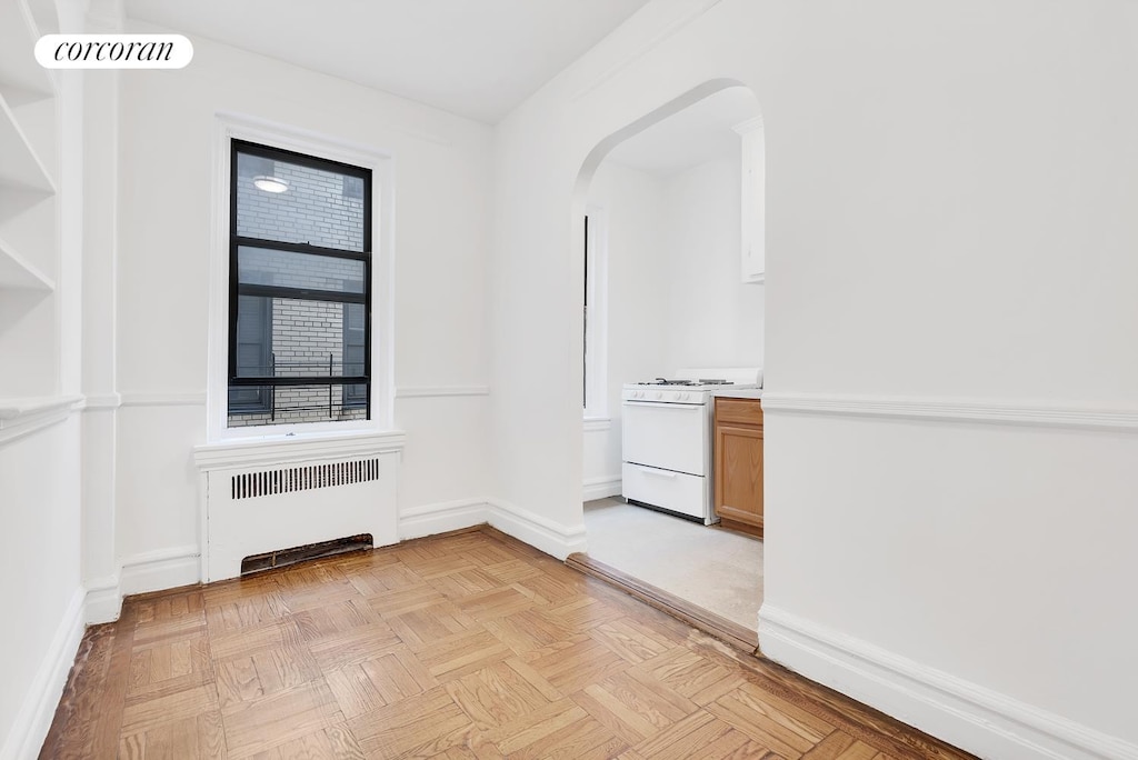 empty room with radiator, baseboards, visible vents, and arched walkways