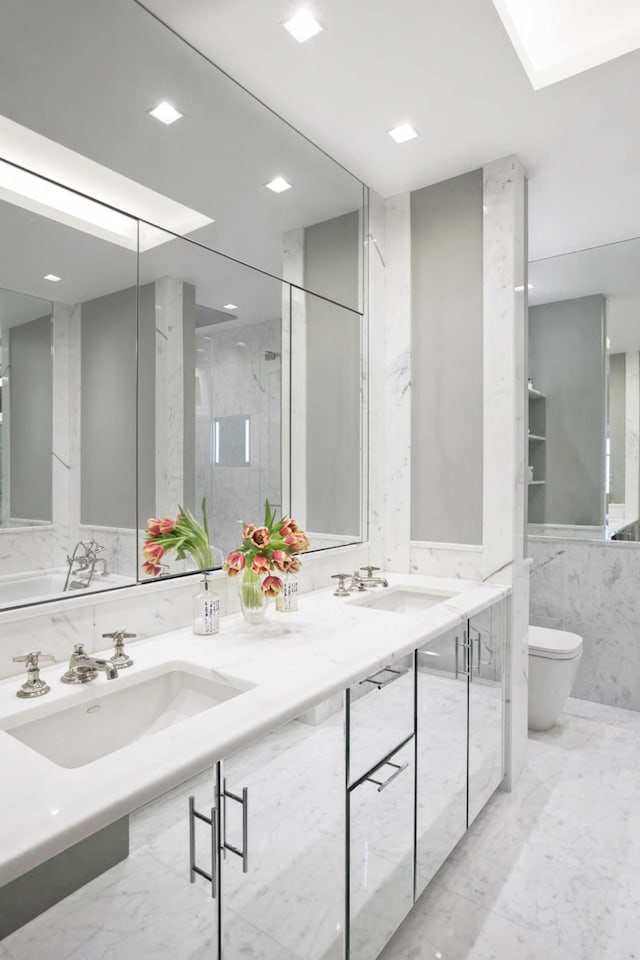 bathroom with toilet, marble finish floor, double vanity, and a sink