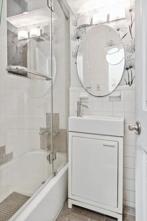 bathroom with tile walls, enclosed tub / shower combo, and vanity