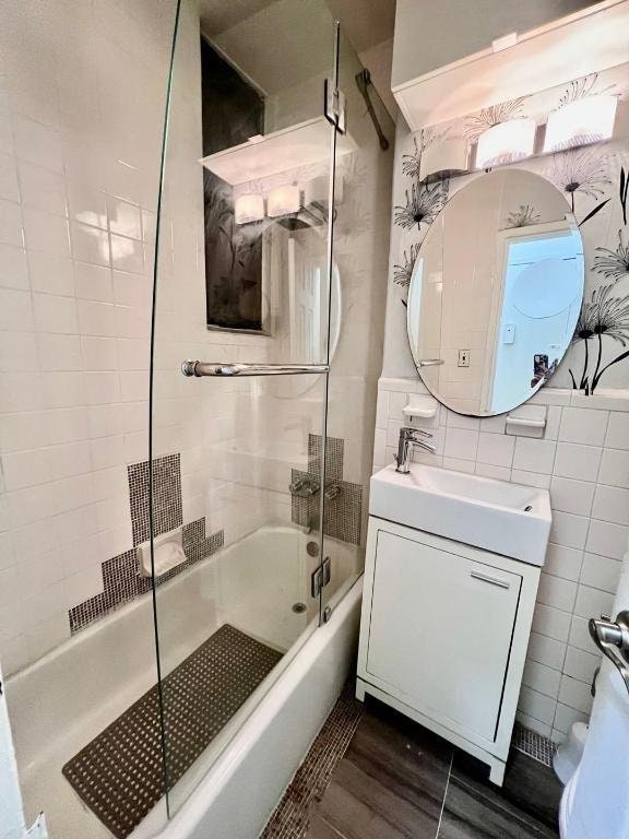 bathroom featuring enclosed tub / shower combo, hardwood / wood-style floors, backsplash, tile walls, and vanity