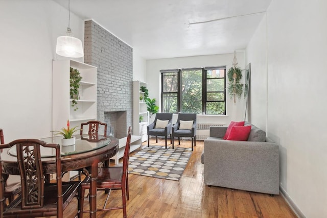 living room featuring a brick fireplace, radiator heating unit, and hardwood / wood-style flooring