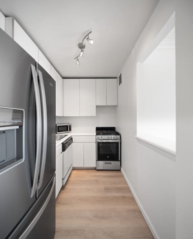 kitchen with rail lighting, white cabinetry, appliances with stainless steel finishes, and light hardwood / wood-style flooring