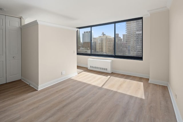 spare room with radiator, crown molding, and light wood-type flooring