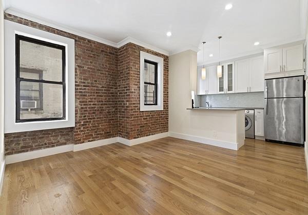 21-48 35th St Unit 4-C, New York City, NY 11105 - kitchen with freestanding refrigerator, washer / clothes dryer, white cabinetry, brick wall, and light wood finished floors