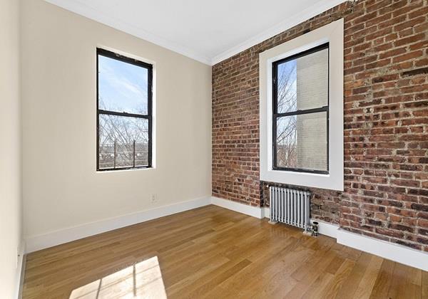 spare room with ornamental molding, radiator, hardwood / wood-style flooring, and brick wall