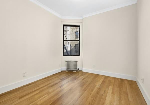 spare room featuring radiator heating unit, wood-type flooring, and ornamental molding