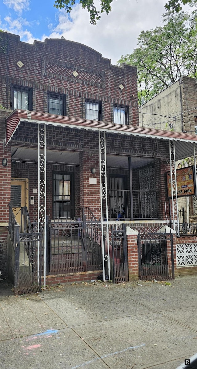multi unit property featuring a gate, brick siding, a porch, and a fenced front yard