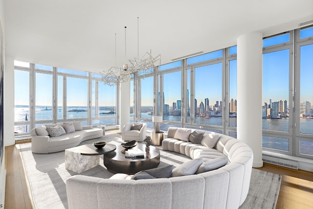 living room with a notable chandelier, light wood-type flooring, a wall of windows, and a water view