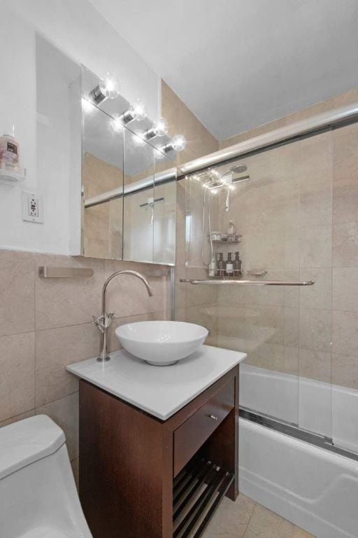 full bathroom featuring shower / bath combination with glass door, tile walls, tile patterned flooring, vanity, and toilet