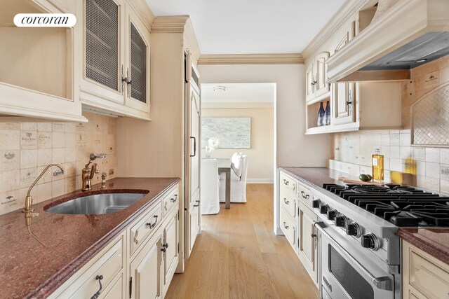 kitchen featuring sink, high end range, light hardwood / wood-style floors, custom range hood, and cream cabinets