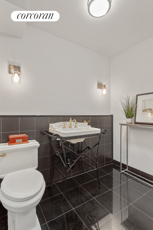 bathroom featuring tile patterned floors, toilet, sink, and tile walls