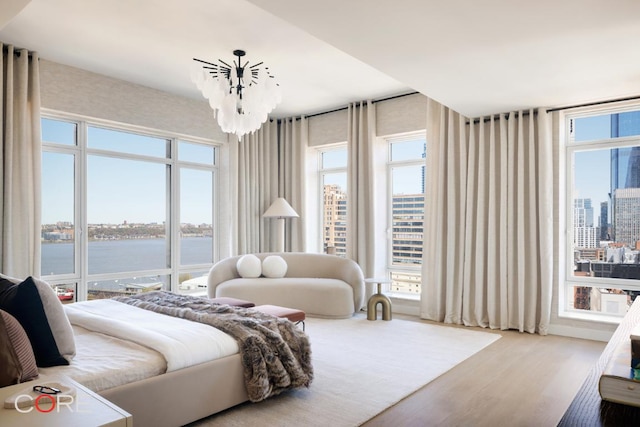 bedroom featuring a water view, an inviting chandelier, and light wood-type flooring