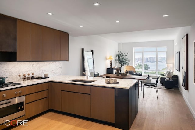 kitchen featuring sink, appliances with stainless steel finishes, kitchen peninsula, light stone countertops, and light hardwood / wood-style floors