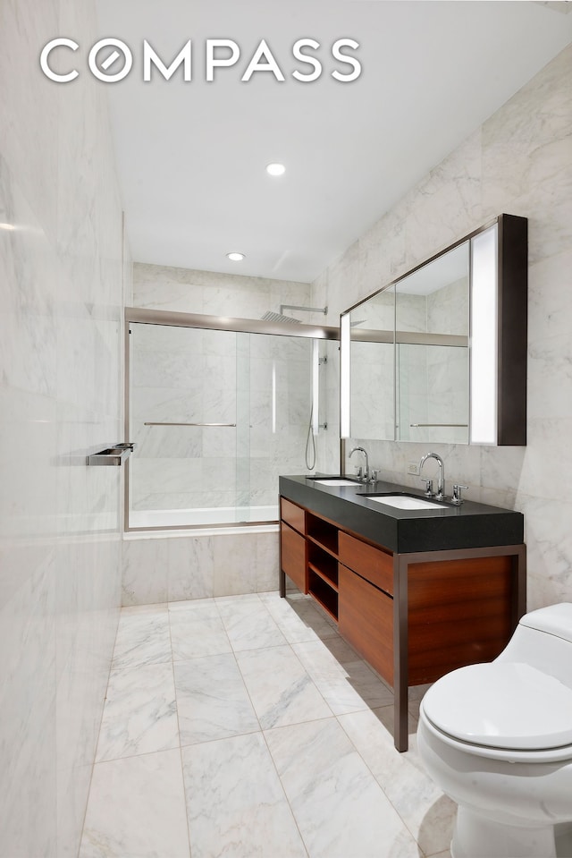full bathroom with toilet, tile walls, marble finish floors, double vanity, and tiled shower / bath combo