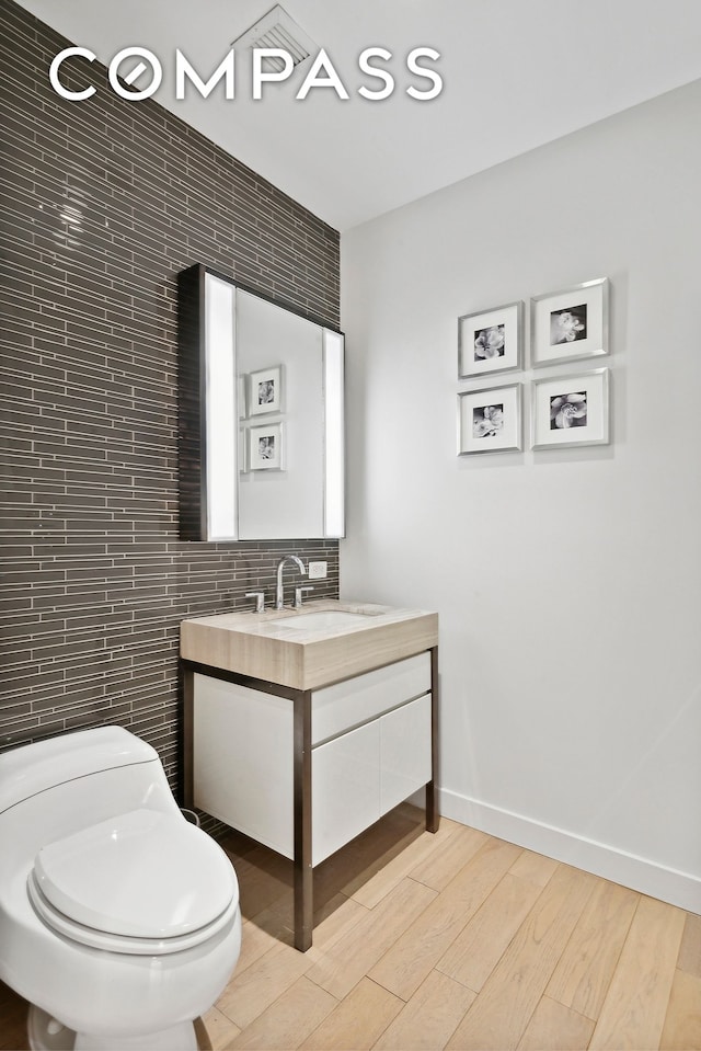 half bathroom featuring wood finished floors, vanity, toilet, tile walls, and baseboards
