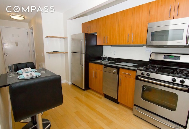 kitchen with dark countertops, brown cabinets, stainless steel appliances, light wood finished floors, and a sink