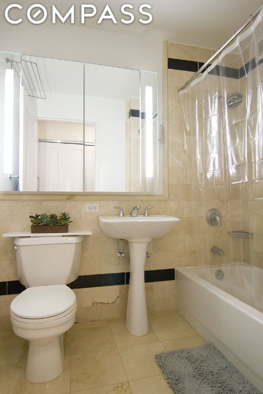 bathroom with shower / bath combo with shower curtain, tile walls, toilet, and tile patterned flooring