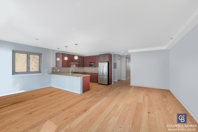 kitchen featuring tasteful backsplash, decorative light fixtures, light wood-type flooring, appliances with stainless steel finishes, and kitchen peninsula