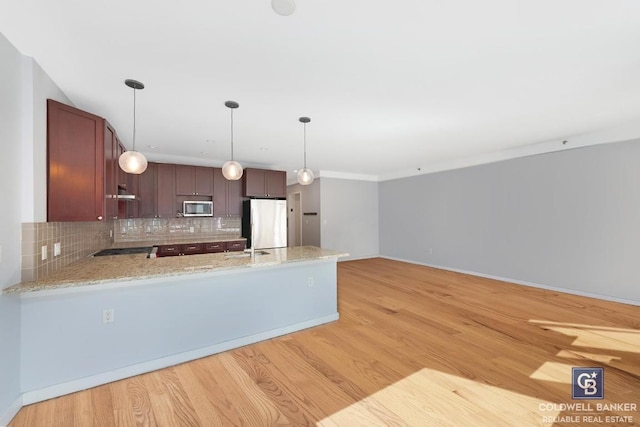 kitchen with pendant lighting, light hardwood / wood-style flooring, appliances with stainless steel finishes, decorative backsplash, and kitchen peninsula