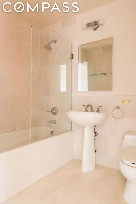 bathroom featuring tile patterned flooring, tiled shower / bath combo, tile walls, and toilet