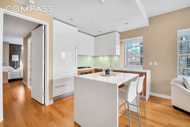 kitchen with white cabinetry, a kitchen breakfast bar, a kitchen island, decorative backsplash, and light wood-type flooring