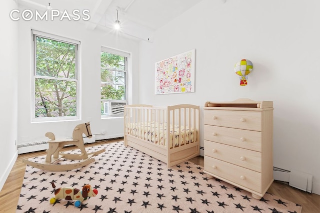 bedroom with cooling unit, a baseboard heating unit, a crib, and light hardwood / wood-style floors