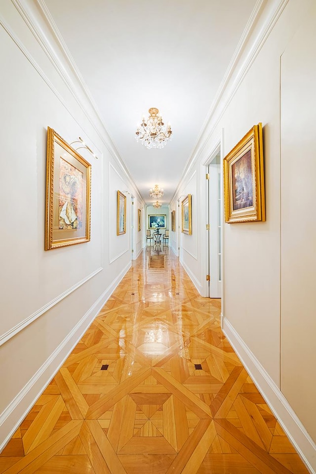 corridor featuring baseboards, a chandelier, crown molding, and a decorative wall