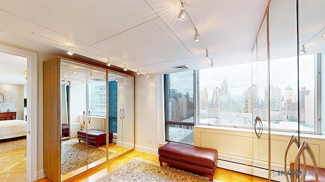 sitting room with visible vents, a city view, track lighting, a baseboard heating unit, and wood finished floors