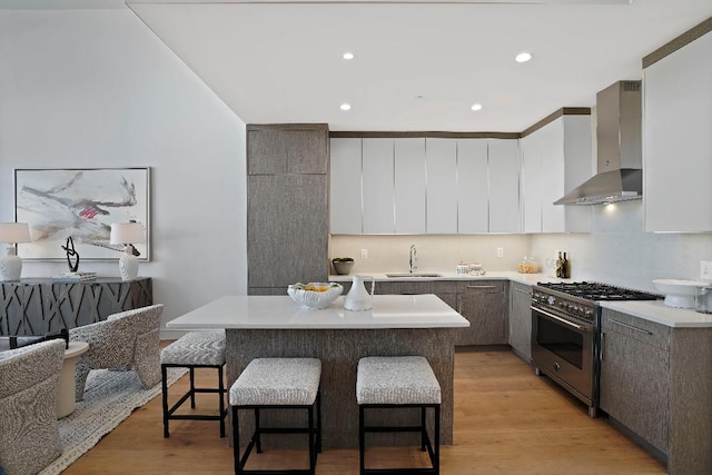 kitchen with wall chimney exhaust hood, a kitchen island, light hardwood / wood-style floors, and stainless steel stove