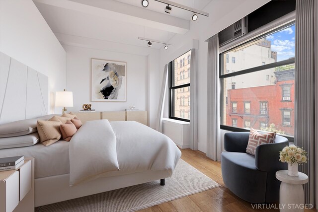 bedroom with track lighting, wood-type flooring, and beam ceiling