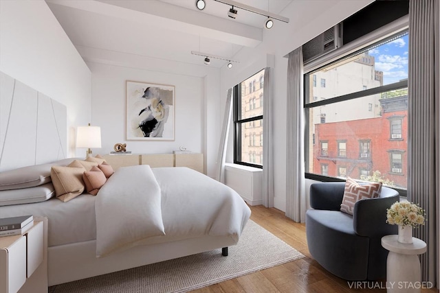 bedroom featuring track lighting, beam ceiling, and light wood finished floors