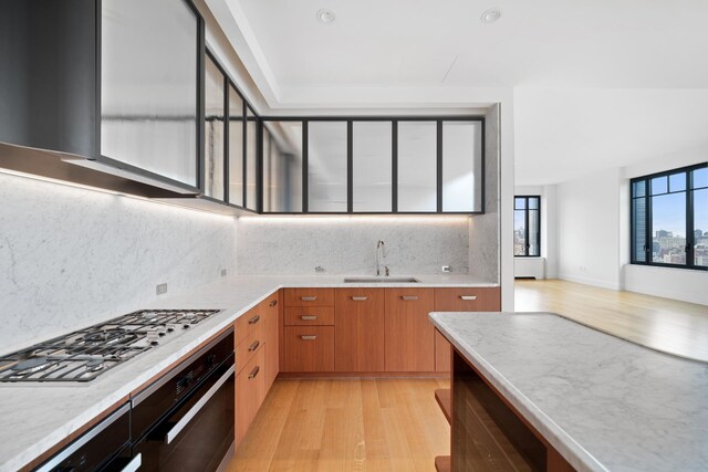 kitchen featuring black oven, stainless steel gas stovetop, sink, decorative backsplash, and light wood-type flooring