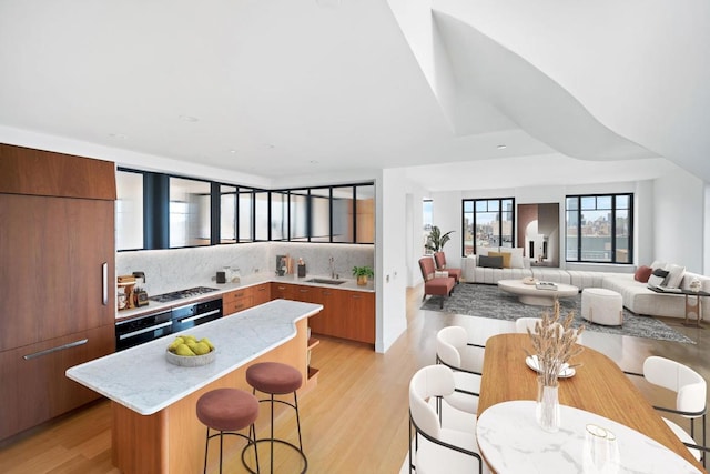 kitchen with a breakfast bar, sink, decorative backsplash, gas cooktop, and light hardwood / wood-style flooring