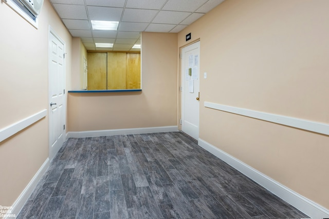 empty room with dark wood-style flooring, a drop ceiling, and baseboards