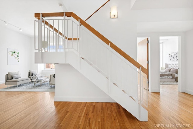 stairway with track lighting, wood-type flooring, and a high ceiling